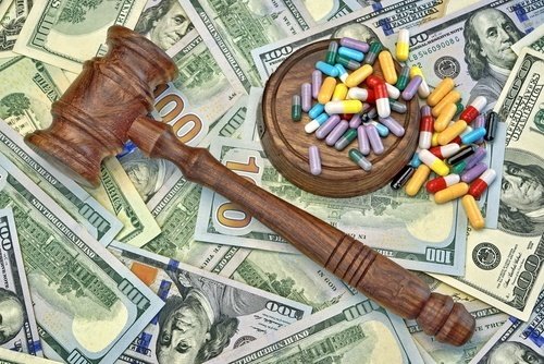 judge's gavel and prescription pills over a layer of $100 bills