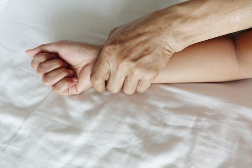 man's hand holding down a woman's hand on bed as an example of sexual assault per Colorado 18-3-402 CRS