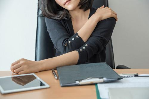 office worker at desk clutching her shoulder