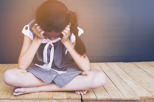 Dejected little girl sitting on floor with her head in her hands. A court will assign her a guardian because her parents cannot take care of her.