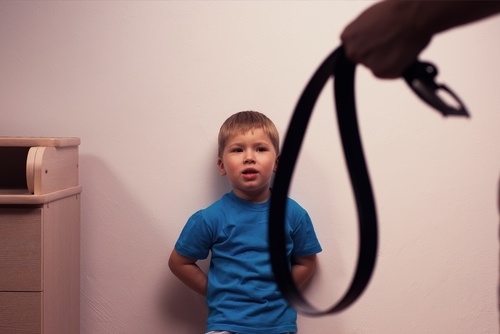 Adult holding belt and young boy looking scared