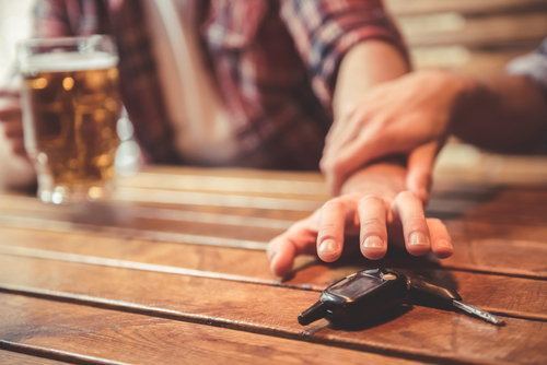 friend holding back the arm of another holding a beer and reaching for his car keys