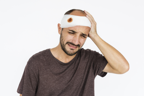 man holding his head which is wrapped in a bloody bandage
