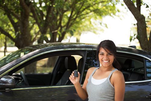 happy Latinx woman holding key in front of car