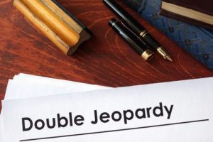 Paper that says "double jeopardy" on a desk with a pen