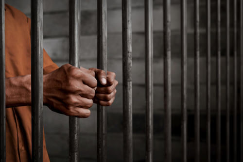 un recluso agarrando las barras de una celda de la cárcel - una violación del Código Penal de California 4550 PC es punible con hasta 4 años de custodia