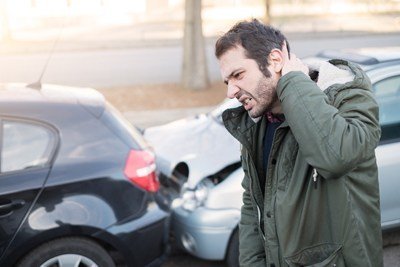 man holding the back of his head in front of two cars that have collided 