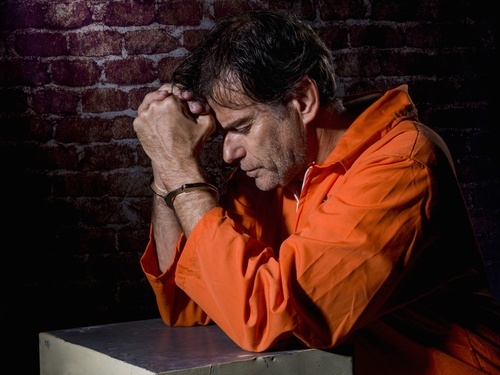 handcuffed prisoner in orange jumpsuit looking sorry for his actions