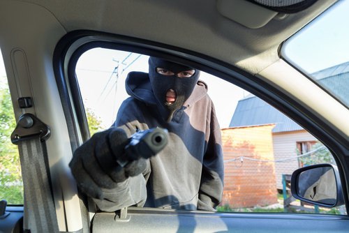 Hombre enmascarado apuntando con un arma a un coche como ejemplo de un carjacking según el Código Penal 215 PC