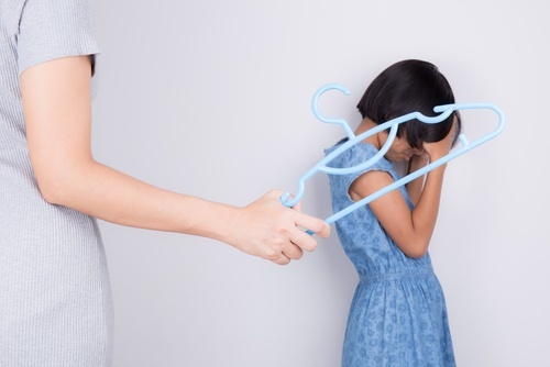 Madre amenazando a su hija pequeña con una percha de plástico para ropa