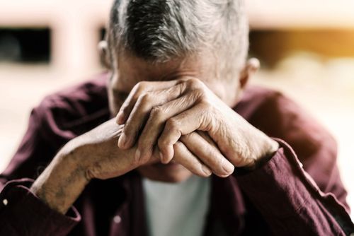 elderly man crouching face into his hands after being abused by a caretaker