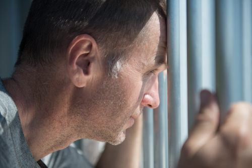 inmate clutching the bars and looking out of a jail cell - a violation of Penal Code 484i PC carries a sentence of up to 3 years