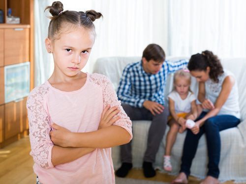 young girl looking jealous while parents talk with her sister