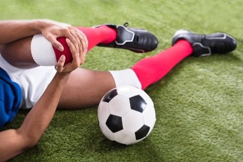 jugador de fútbol joven acostado en el campo agarrando la rodilla las lesiones deportivas en la escuela pueden dar lugar a una demanda por daños y perjuicios