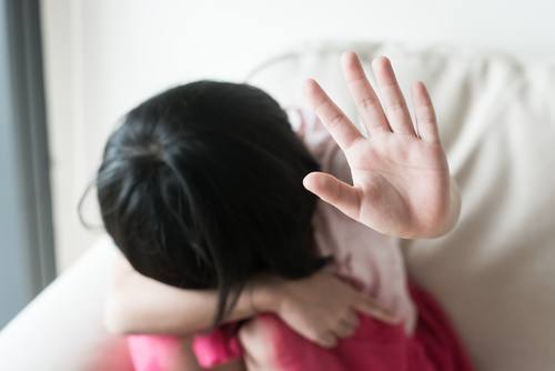 scared child hiding her head and holding her hand up in "stop" gesture