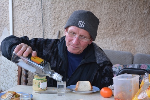 Senior man in wooly hat pouring himself a glass of vodka. He was assigned a guardian because he can no longer care for himself.