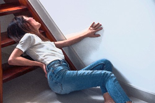 woman clutching her lower back at the bottom of a staircase - stairway accidents often lead to premises liability claims in California