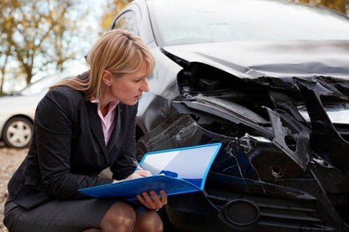female insurance adjuster inspecting damaged car