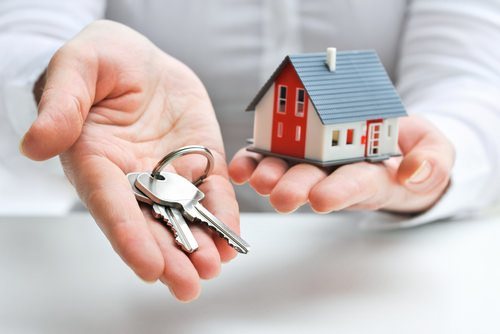 one hand holding keys and the other hand holding a model house