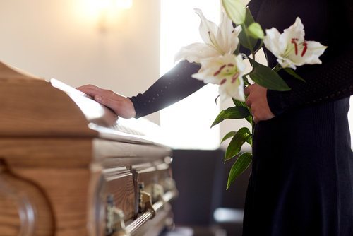 woman holding lilies and touching a casket holding victim of a wrongful death
