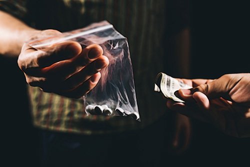 man handing a bag of pills in exchange for cash as an example of sale of a controlled substance per California Health & Safety Code 11352 HS