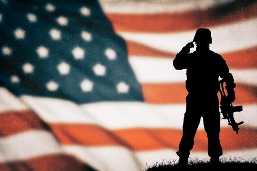 Silhouette of soldier in combat gear standing in front of American flag - military diversion is an option for veterans in some California criminal cases