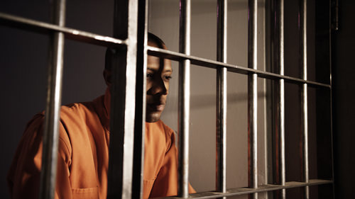 un recluso en un mono naranja mirando desde una celda de prisión - una condena bajo el Código Penal 499b PC puede llevar a multas y prisión