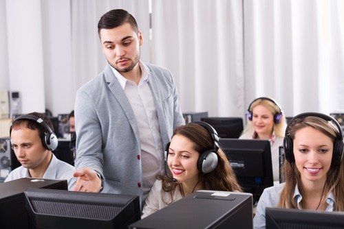 male boss in suit supervising receptionists in headsets