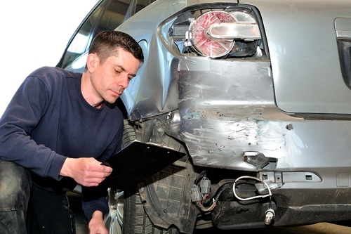 man with clipboard examining wrecked car