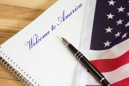 pen lying on top of flag and notepad that reads "Welcome to America"