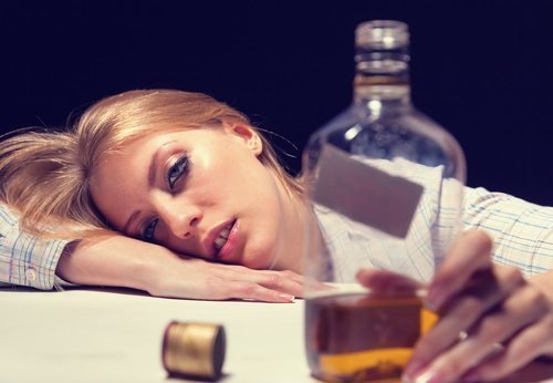 woman intoxicated with hand on a bottle of whiskey
