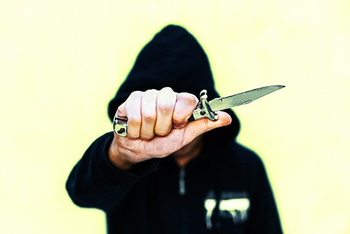 hooded man holding switchblade with the blade extended as an example of a Penal Code 21510 PC violation