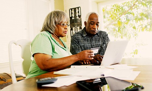 personas mayores escribiendo su número de tarjeta de crédito en su computadora portátil - el abuso financiero de ancianos es un delito grave en California