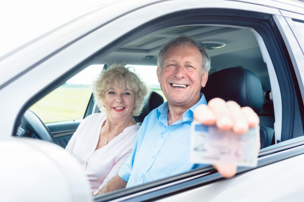 Elderly drivers flashing their license in a car.