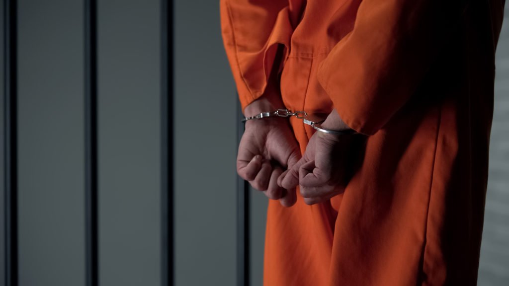 Hombre con mono naranja esposado en una celda de prisión: una condena por pornografía infantil bajo el Código Penal 311.11 PC conlleva hasta 3 años de custodia