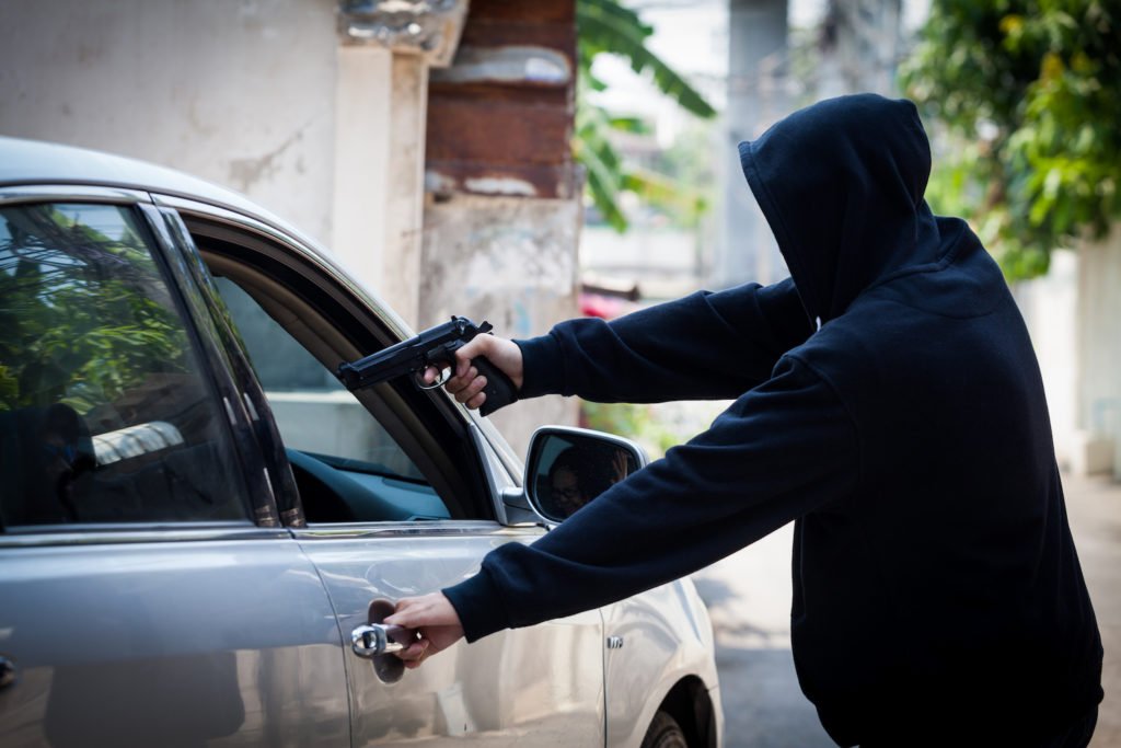 Hooded carjacker pointing gun into vehicle
