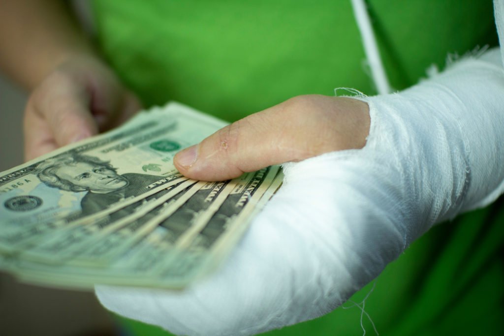 Hombre con brazo en yeso sosteniendo una bola de billetes de $20 para ejemplificar los daños compensatorios en California