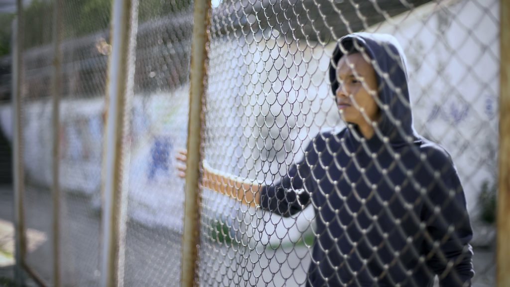 Niño truant en sudadera detrás de una reja