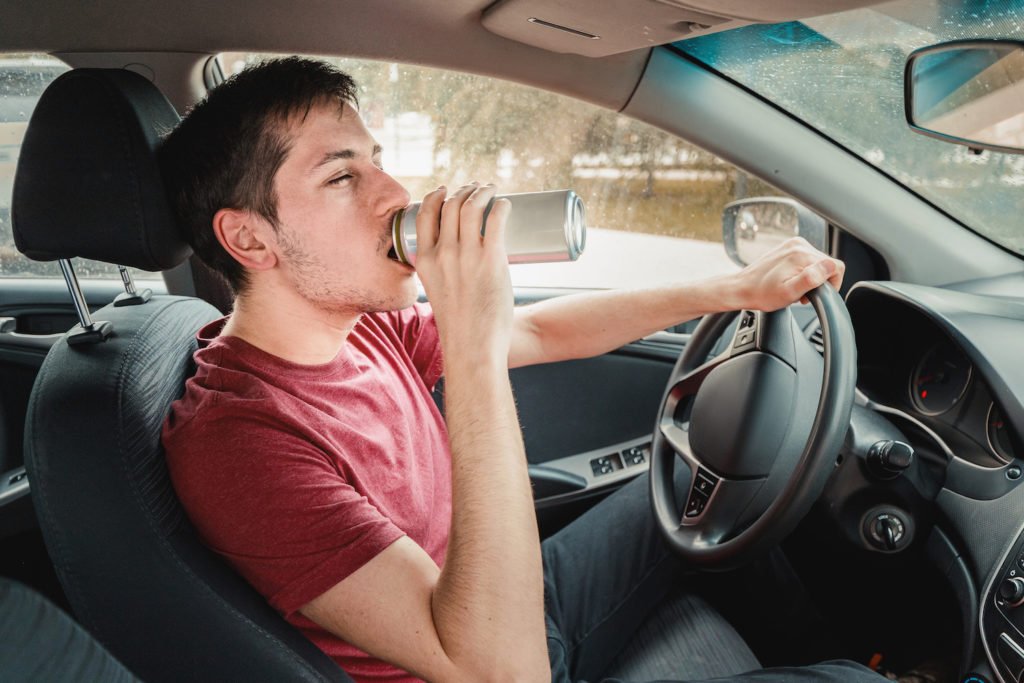 Intoxicated young man drinking beer while behind the wheel on the road and an example a Vehicle Code 23152(a) VC violation