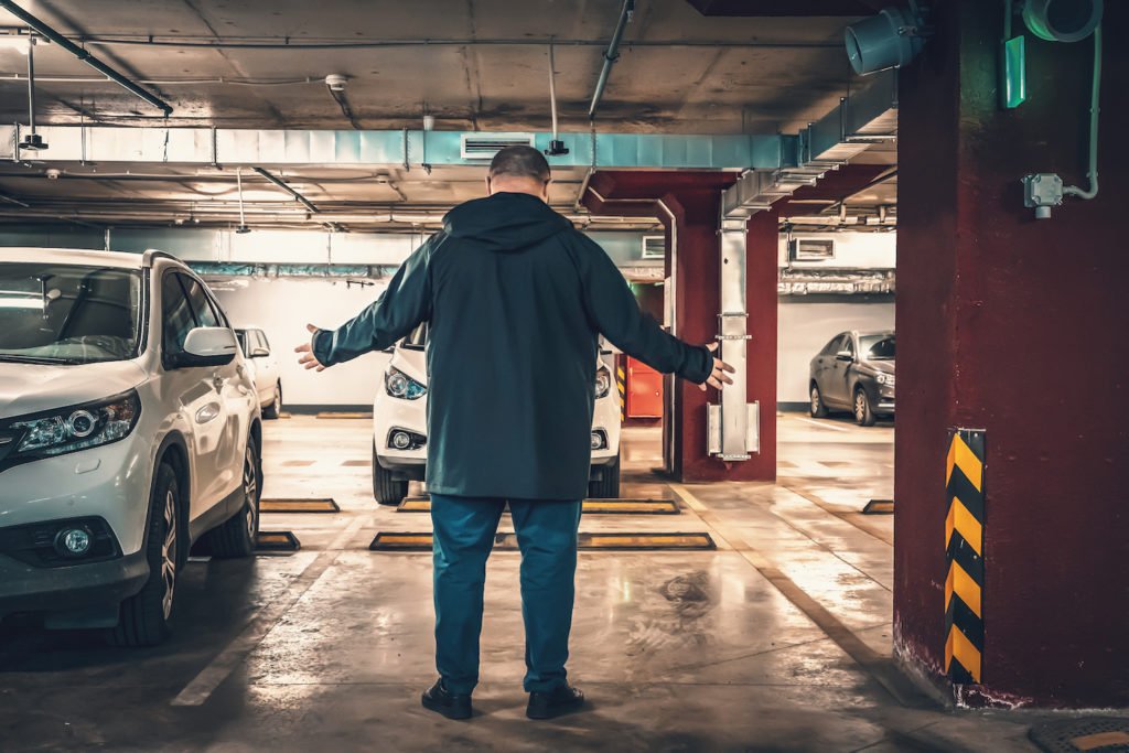Hombre de pie en un espacio de estacionamiento vacío en un garaje subterráneo: hacer un informe falso de robo de auto es un delito en California