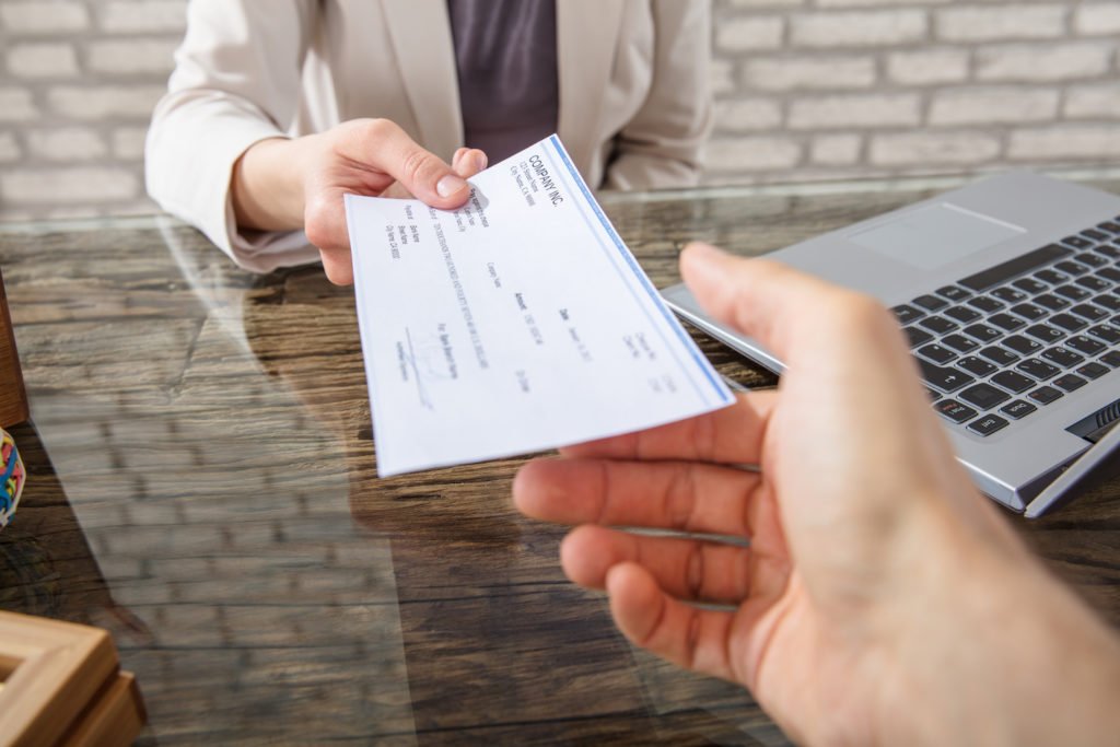 Primer plano de un empleador entregando un cheque al empleado