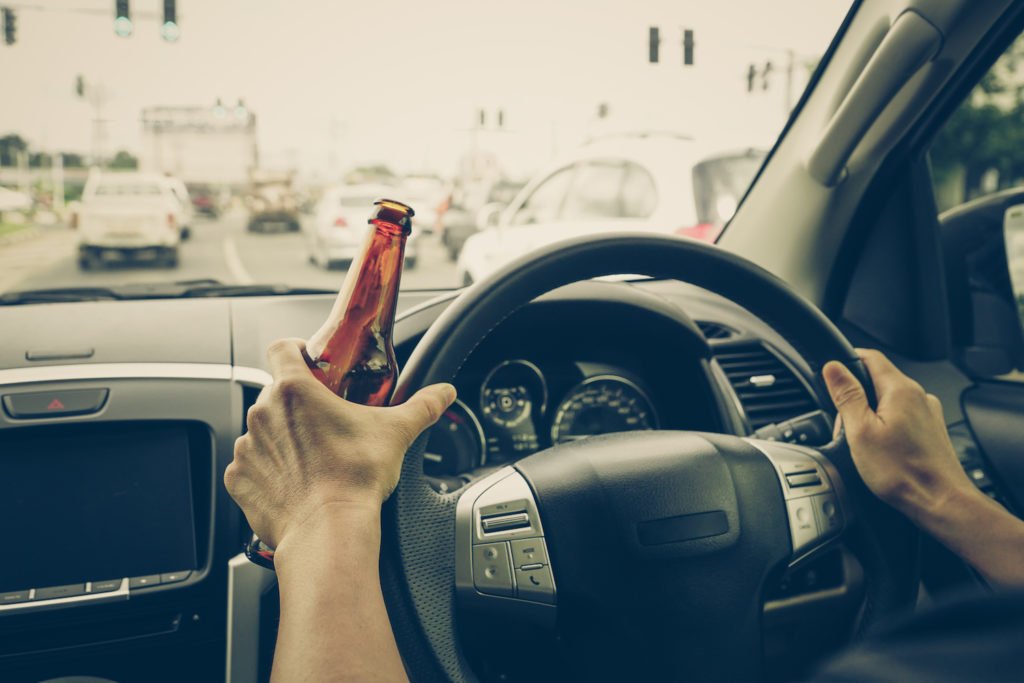 Hands on car wheel while holding beer bottle