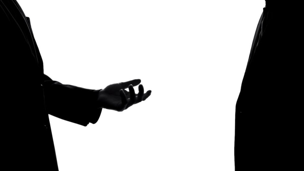 Silhouette of two people, with one person's hand reaching out in a menacing way to the other to illustrate attempted extortion