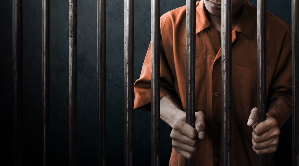 Un condenado bajo libertad condicional con un mono naranja detrás de barrotes