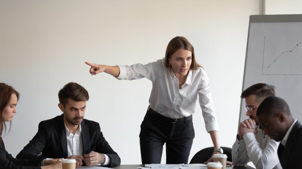 Angry white boss singling out black employee during board meeting.