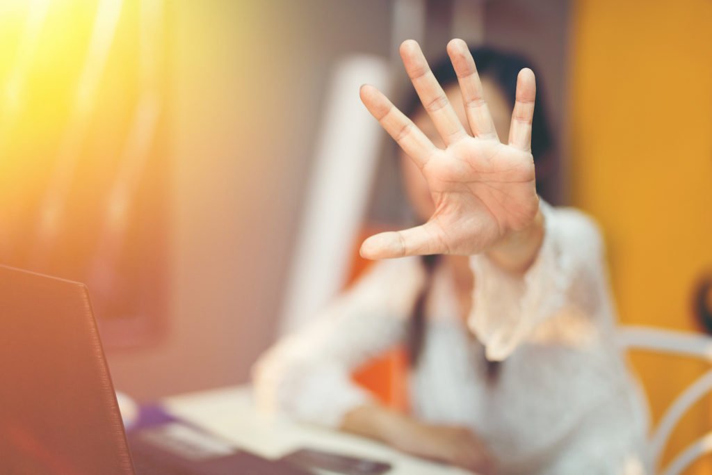 Mujer en escritorio de trabajo sosteniendo la mano para defenderse de un ataque