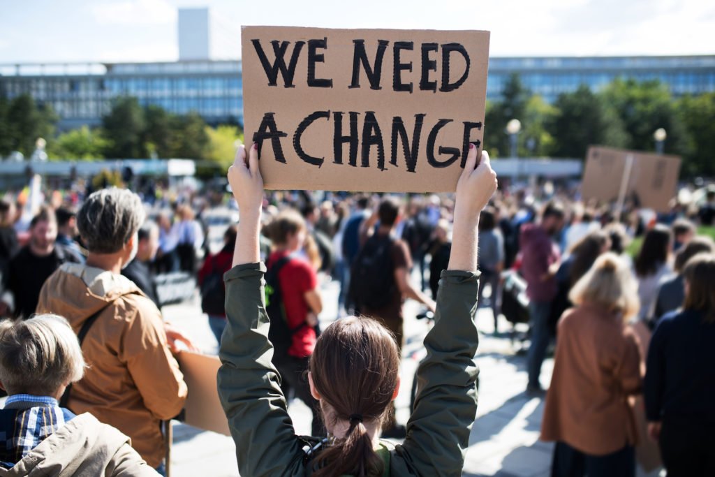 Political protester holding a sign that says 'We Need a Change', which would not be a legal ground to fire the protester in California
