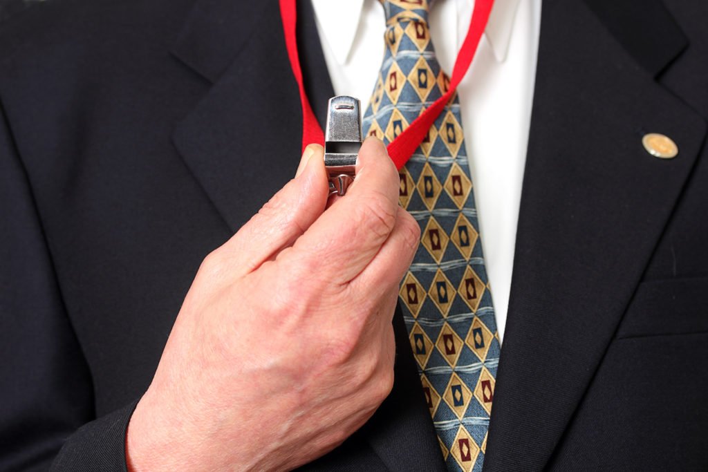 Closeup of man's hand holding up a whistle - firing a whistleblower can constitute wrongful termination in California