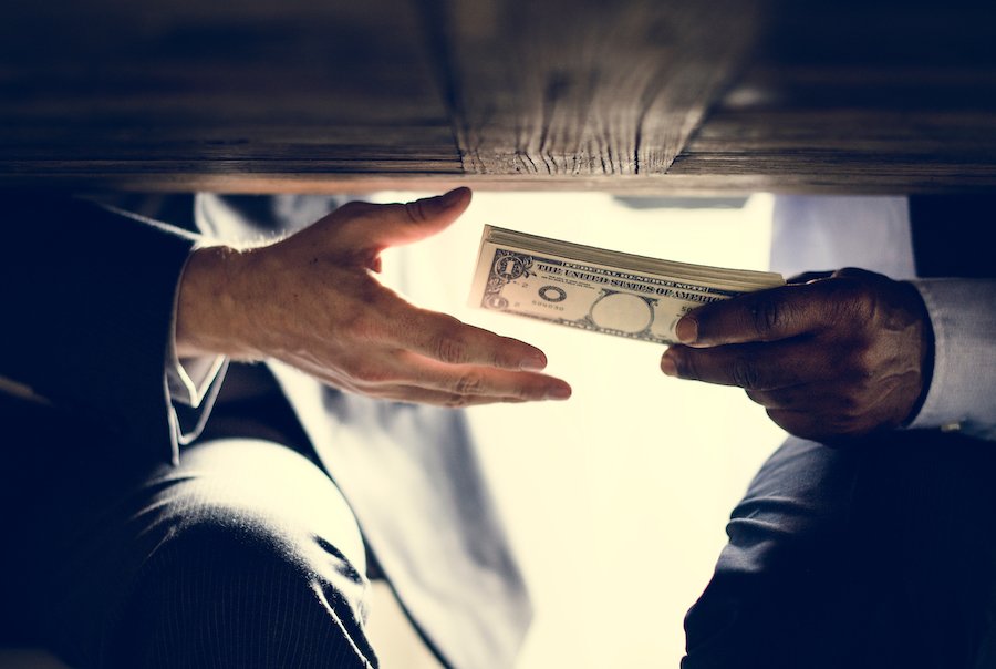 Hand handing money to another hand under a table