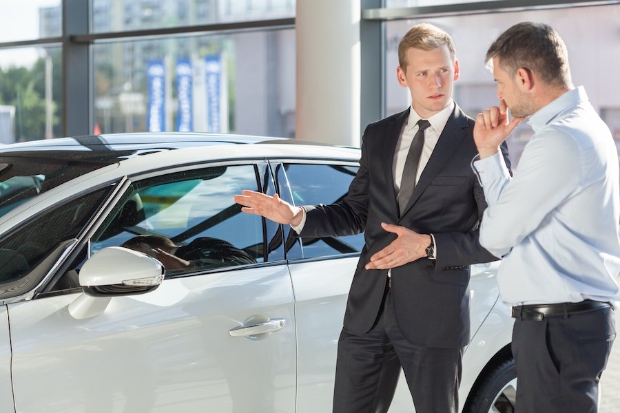 Vendedor de automóviles con cliente frente a un sedán